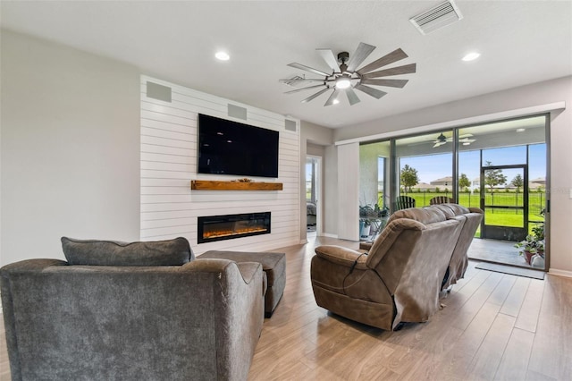 living room with a fireplace, wood walls, light wood-type flooring, and ceiling fan