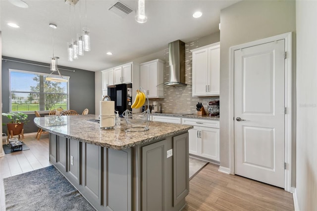 kitchen featuring light wood-type flooring, white cabinets, an island with sink, wall chimney exhaust hood, and decorative backsplash