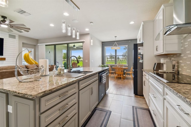 kitchen with ceiling fan, light wood-type flooring, wall chimney exhaust hood, a center island with sink, and backsplash