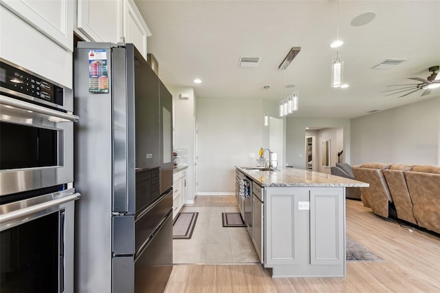 kitchen with ceiling fan, stainless steel appliances, sink, a center island with sink, and light hardwood / wood-style floors