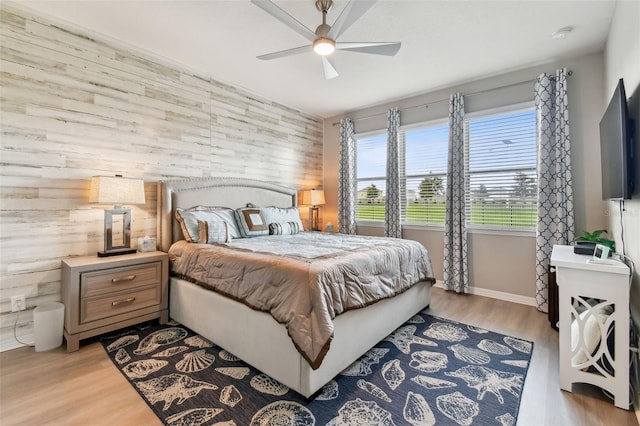 bedroom with ceiling fan, light wood-type flooring, and wooden walls