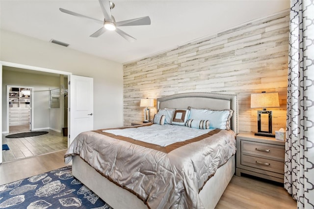 bedroom featuring ceiling fan, light wood-type flooring, and wooden walls