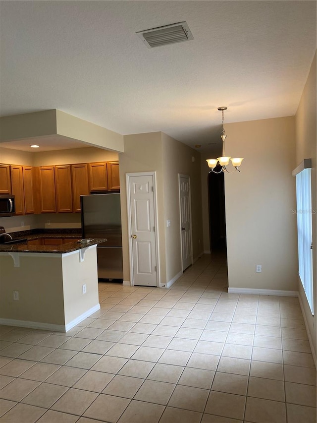 kitchen with visible vents, black fridge, brown cabinetry, dark countertops, and decorative light fixtures