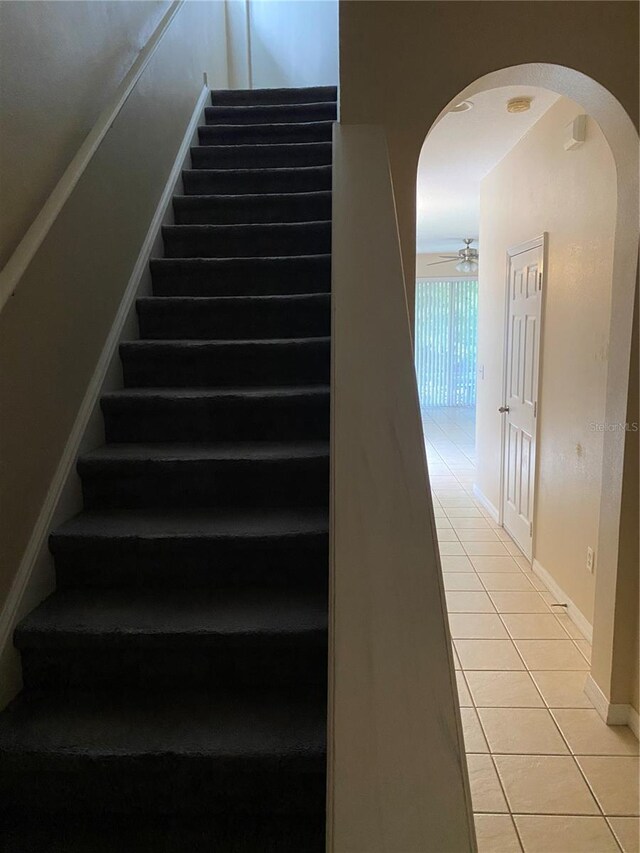 stairway with arched walkways, tile patterned flooring, a ceiling fan, and baseboards