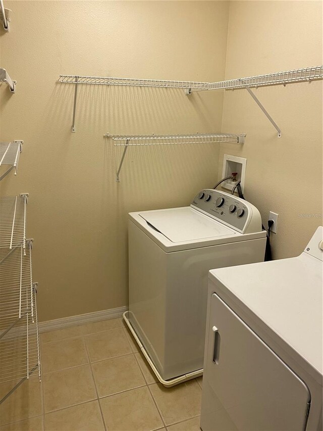 clothes washing area with light tile patterned floors, laundry area, baseboards, and washer and dryer