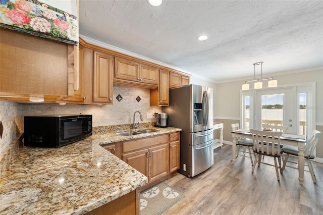 kitchen featuring light stone countertops, sink, hanging light fixtures, stainless steel fridge, and ornamental molding