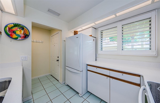 kitchen with white cabinetry, white fridge, light tile patterned floors, and range