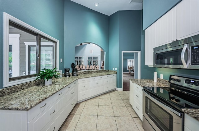 kitchen with light stone counters, light tile patterned floors, appliances with stainless steel finishes, white cabinets, and a high ceiling