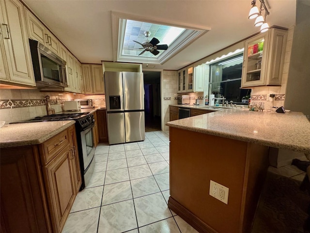 kitchen featuring ceiling fan, kitchen peninsula, sink, appliances with stainless steel finishes, and light stone counters