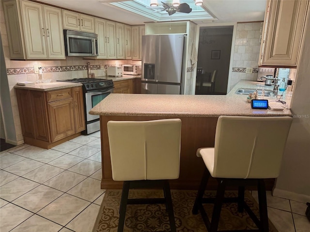 kitchen with stainless steel appliances, tasteful backsplash, kitchen peninsula, light tile patterned flooring, and a breakfast bar