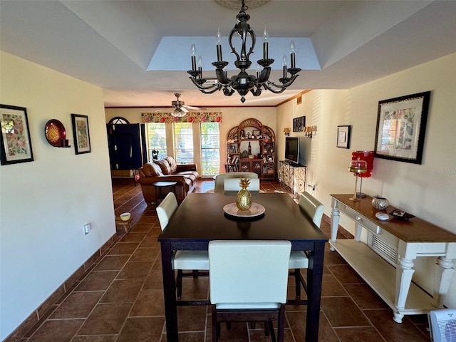 tiled dining area featuring ceiling fan with notable chandelier and a tray ceiling