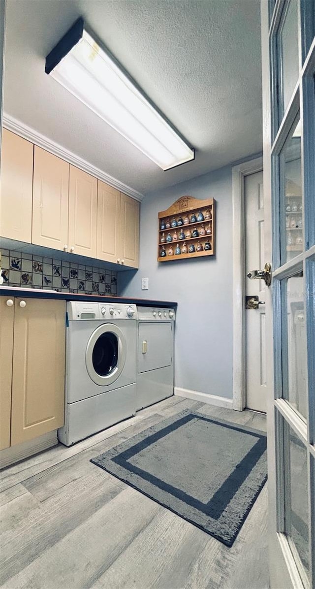 clothes washing area with light hardwood / wood-style floors, cabinets, a textured ceiling, and washer and clothes dryer