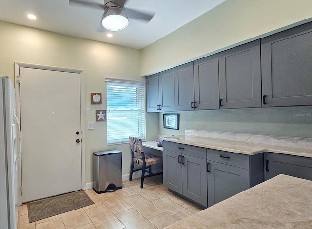 kitchen with built in desk, gray cabinetry, white refrigerator with ice dispenser, light tile patterned floors, and ceiling fan