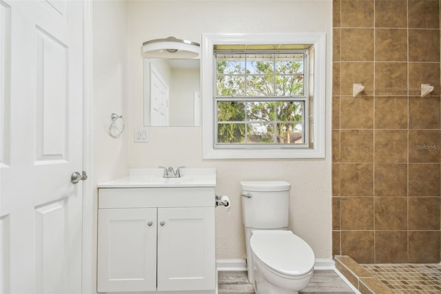 bathroom with hardwood / wood-style floors, vanity, toilet, and tiled shower