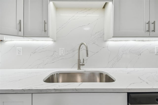 kitchen featuring backsplash, light stone counters, white cabinetry, and sink