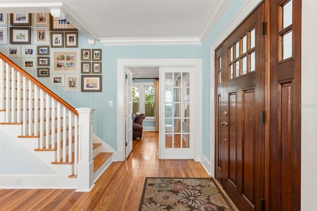 foyer entrance with light hardwood / wood-style flooring, ornamental molding, and french doors