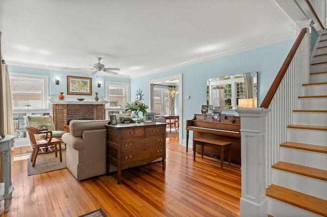 living room featuring a brick fireplace, ceiling fan with notable chandelier, crown molding, and hardwood / wood-style floors