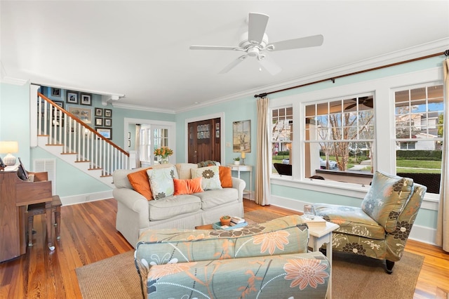 living room featuring baseboards, a ceiling fan, ornamental molding, stairs, and light wood-style floors