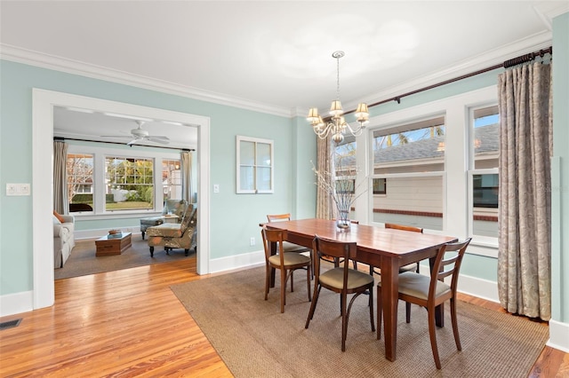 dining room with crown molding, visible vents, light wood-type flooring, baseboards, and ceiling fan with notable chandelier