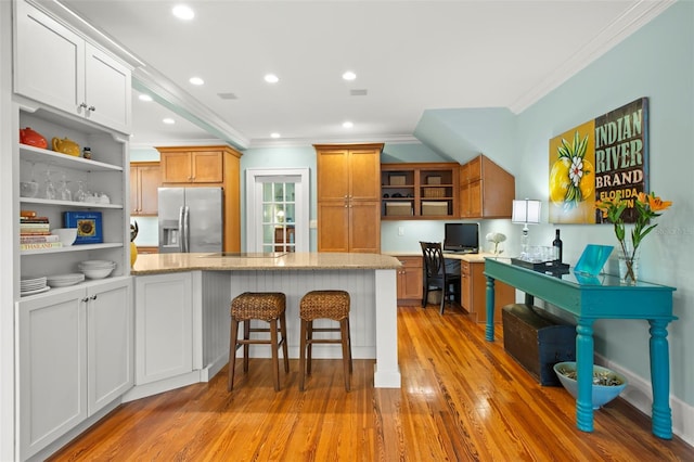 kitchen with white cabinetry, brown cabinets, open shelves, stainless steel fridge, and a kitchen bar