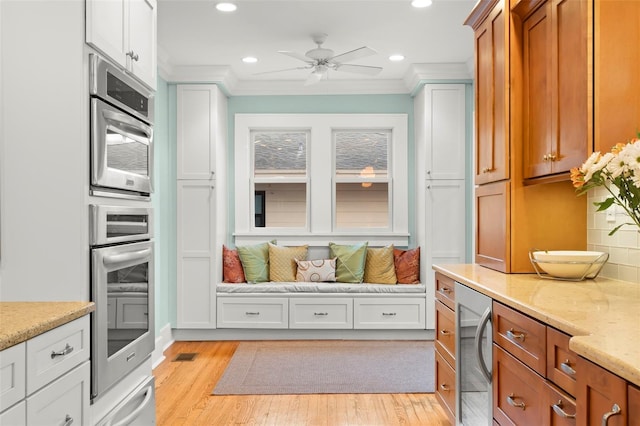 kitchen with brown cabinetry, white cabinets, ornamental molding, and light stone countertops