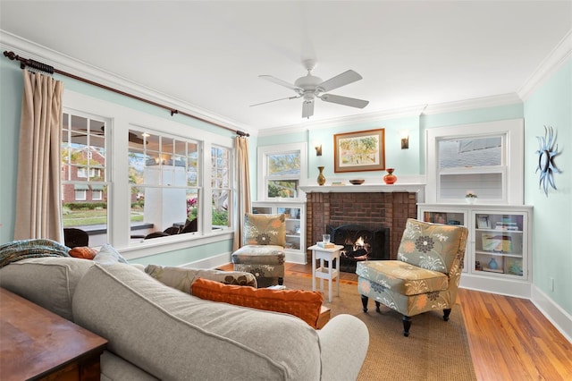 sitting room featuring ceiling fan, a fireplace, baseboards, light wood-style floors, and crown molding