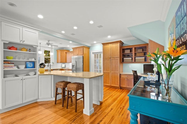 kitchen with a breakfast bar, open shelves, white cabinets, light stone countertops, and stainless steel fridge