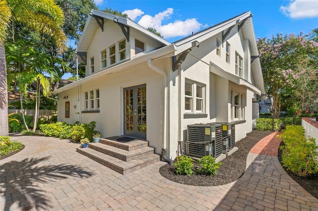 view of side of home featuring cooling unit, french doors, fence, and stucco siding