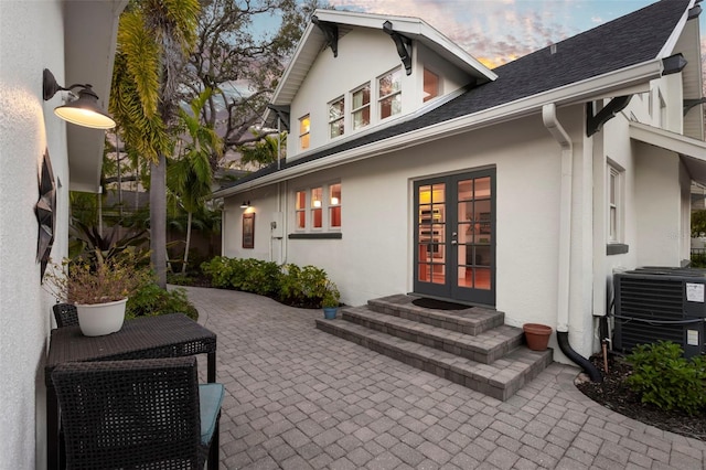 back of house at dusk featuring central AC, french doors, a patio area, and stucco siding