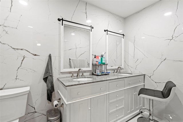 bathroom with dual vanity, toilet, and tile walls