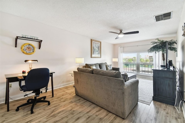 living room featuring ceiling fan, a textured ceiling, and light wood-type flooring