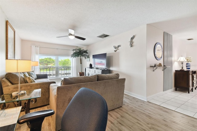 living room featuring ceiling fan, light hardwood / wood-style flooring, and a textured ceiling