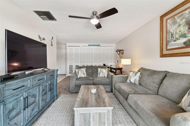 living room featuring a textured ceiling, light hardwood / wood-style flooring, and ceiling fan