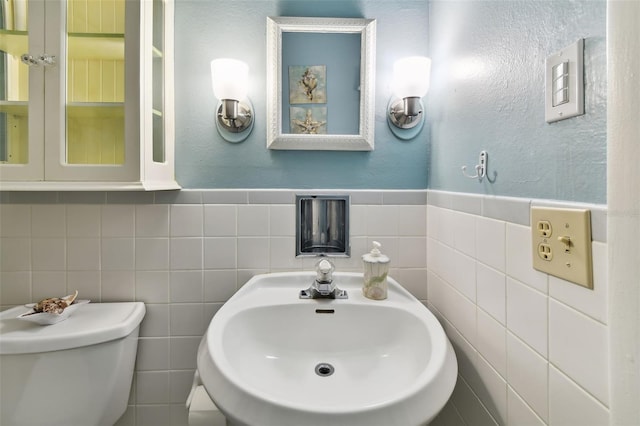 bathroom with toilet, sink, and tile walls