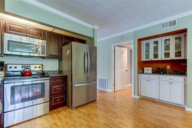 kitchen featuring light hardwood / wood-style flooring, a textured ceiling, dark stone counters, ornamental molding, and stainless steel appliances