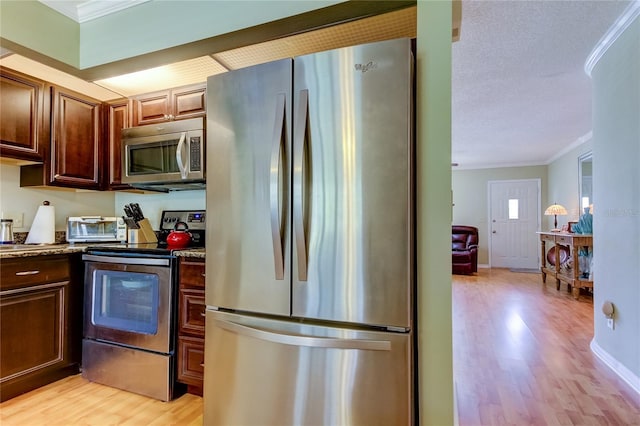 kitchen featuring light hardwood / wood-style flooring, a textured ceiling, ornamental molding, appliances with stainless steel finishes, and light stone countertops