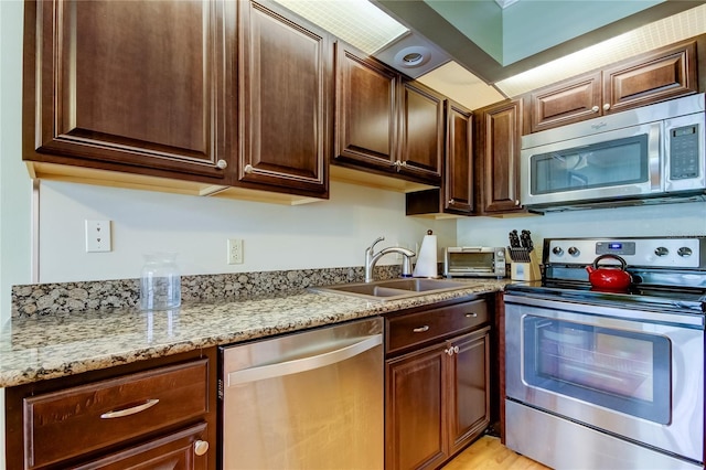 kitchen with dark brown cabinetry, sink, light stone countertops, and appliances with stainless steel finishes