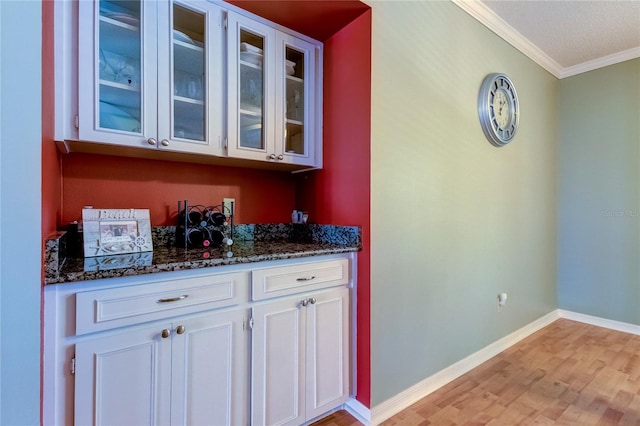 bar with crown molding, light hardwood / wood-style floors, and white cabinets