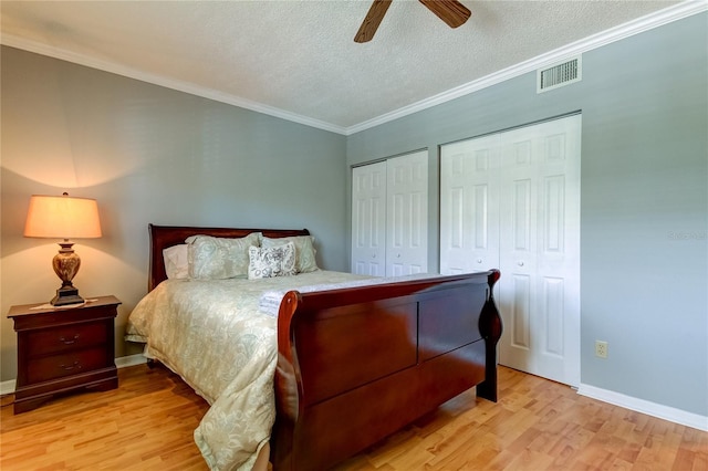 bedroom featuring ornamental molding, ceiling fan, light hardwood / wood-style floors, multiple closets, and a textured ceiling