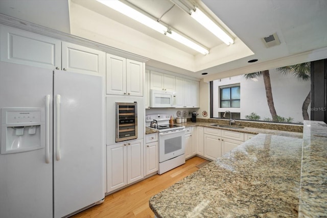 kitchen with beverage cooler, white appliances, a sink, light wood-style floors, and a tray ceiling