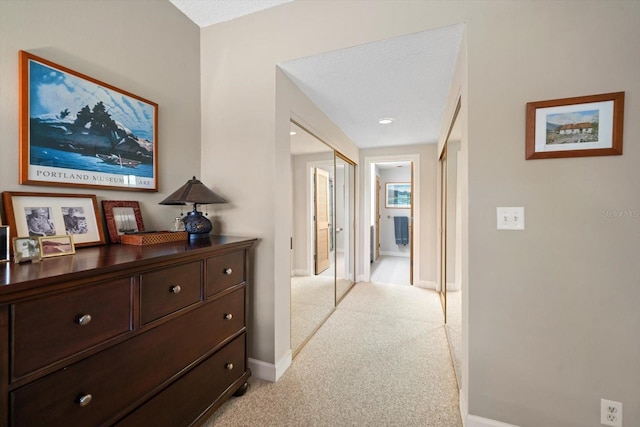 hallway with baseboards and light colored carpet