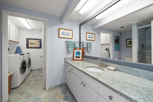 full bath featuring washer and clothes dryer, a stall shower, stone finish flooring, vanity, and baseboards