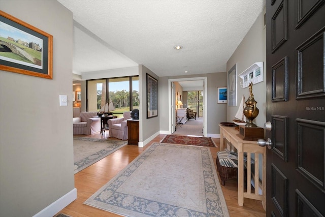 entryway with light wood-type flooring, baseboards, and a textured ceiling