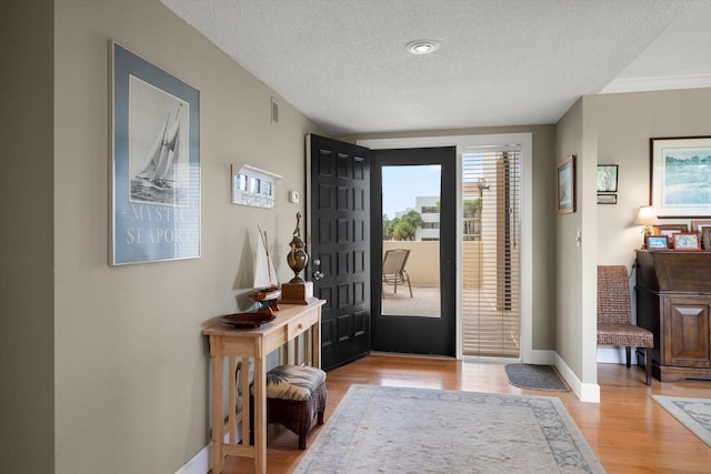 foyer featuring light wood-style floors, visible vents, a textured ceiling, and baseboards