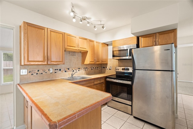 kitchen featuring tasteful backsplash, light tile patterned floors, sink, kitchen peninsula, and stainless steel appliances