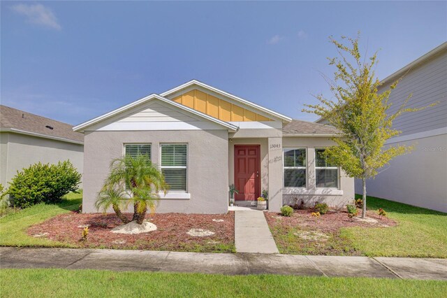 view of front of property with board and batten siding, a front yard, and stucco siding