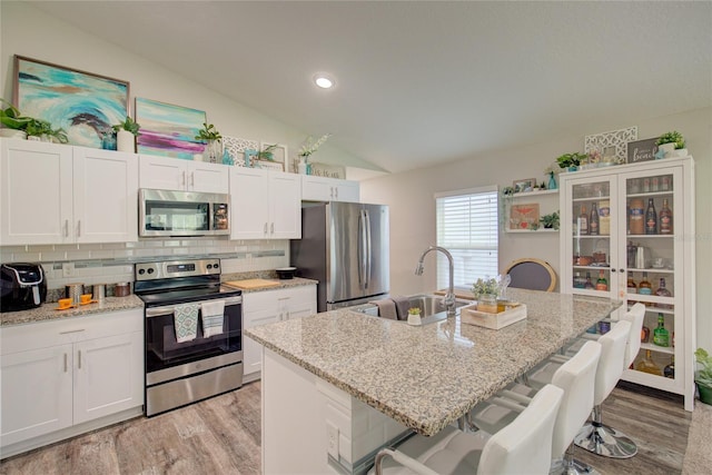 kitchen featuring white cabinets, appliances with stainless steel finishes, light stone counters, a kitchen island with sink, and a kitchen bar