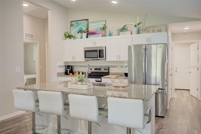 kitchen featuring vaulted ceiling, a center island with sink, appliances with stainless steel finishes, and white cabinets