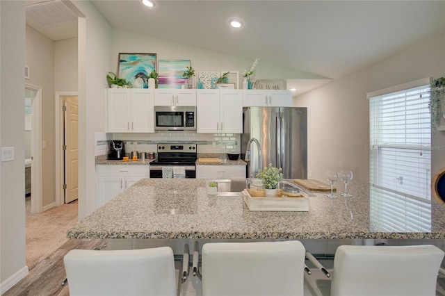 kitchen featuring lofted ceiling, appliances with stainless steel finishes, a breakfast bar area, and white cabinetry