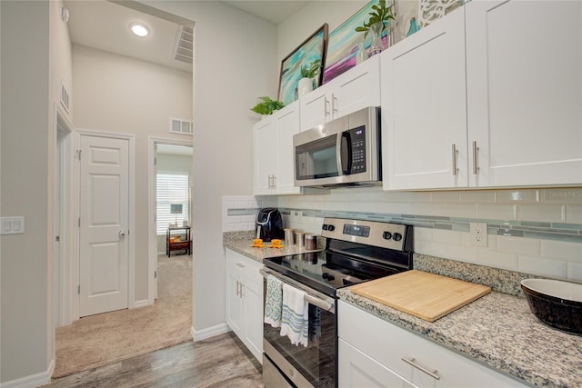 kitchen with light stone countertops, visible vents, white cabinetry, and stainless steel appliances